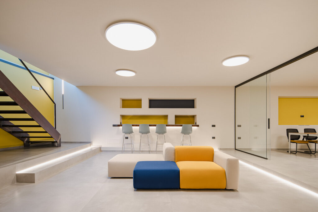 Area lounge contemporanea con divano modulare colorato, scala e pareti vetrate