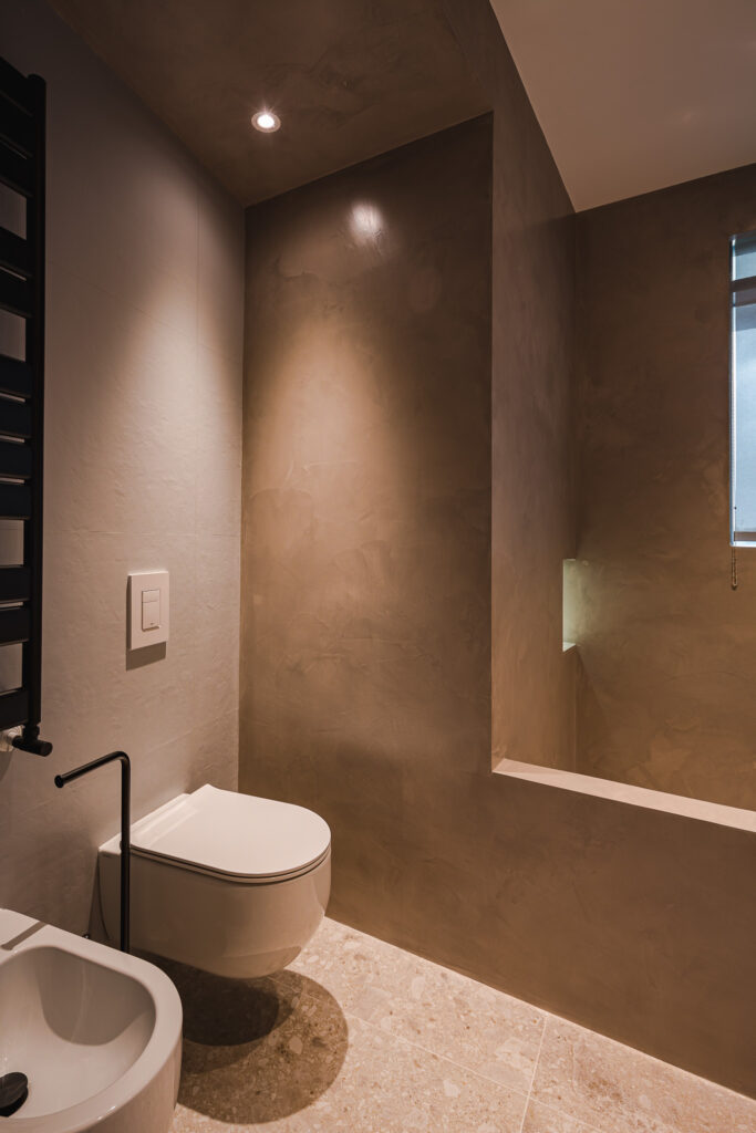 Sanitari sospesi e zona doccia con nicchia illuminata e pareti color tortora