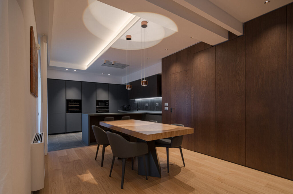 Sala da pranzo con grande tavolo, cucina nera e parete in legno