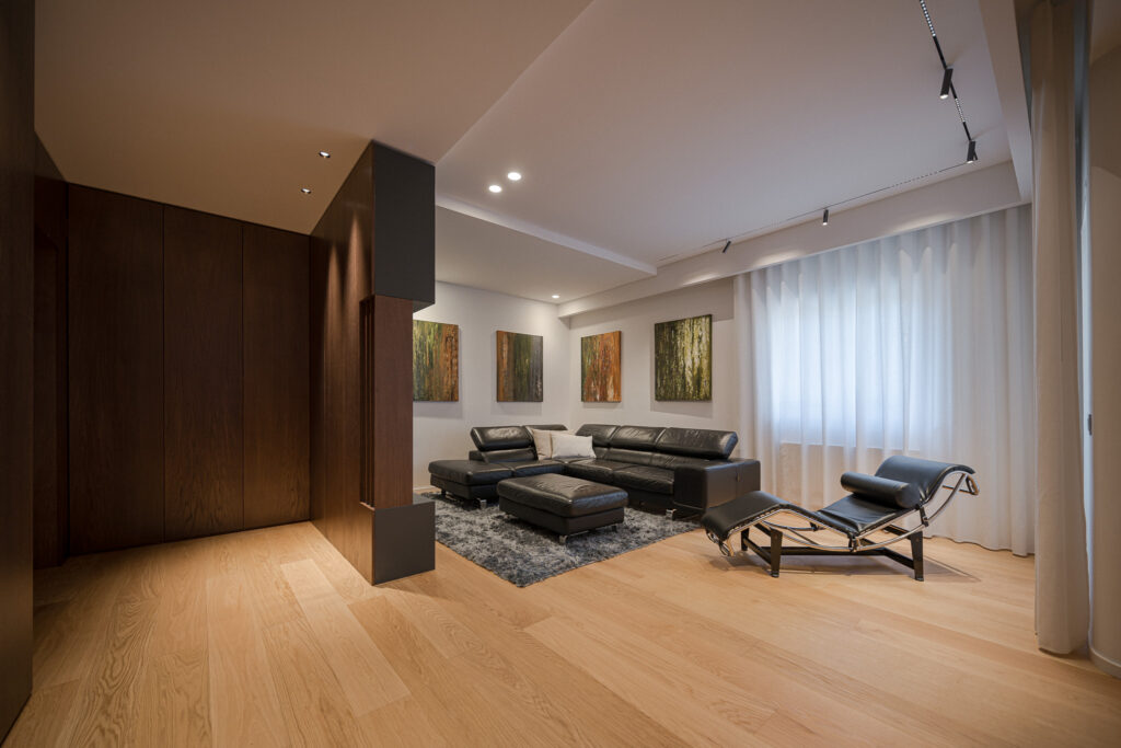 Ampio soggiorno con parquet, divano nero e parete attrezzata in legno