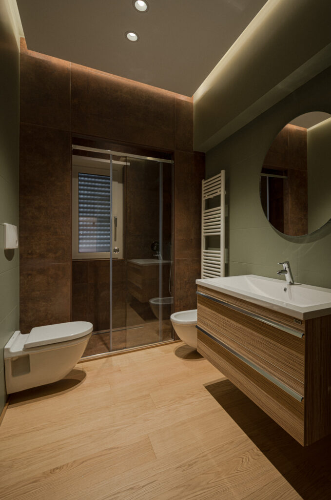 Bagno con pareti verdi, mobile lavabo in legno e doccia in vetro