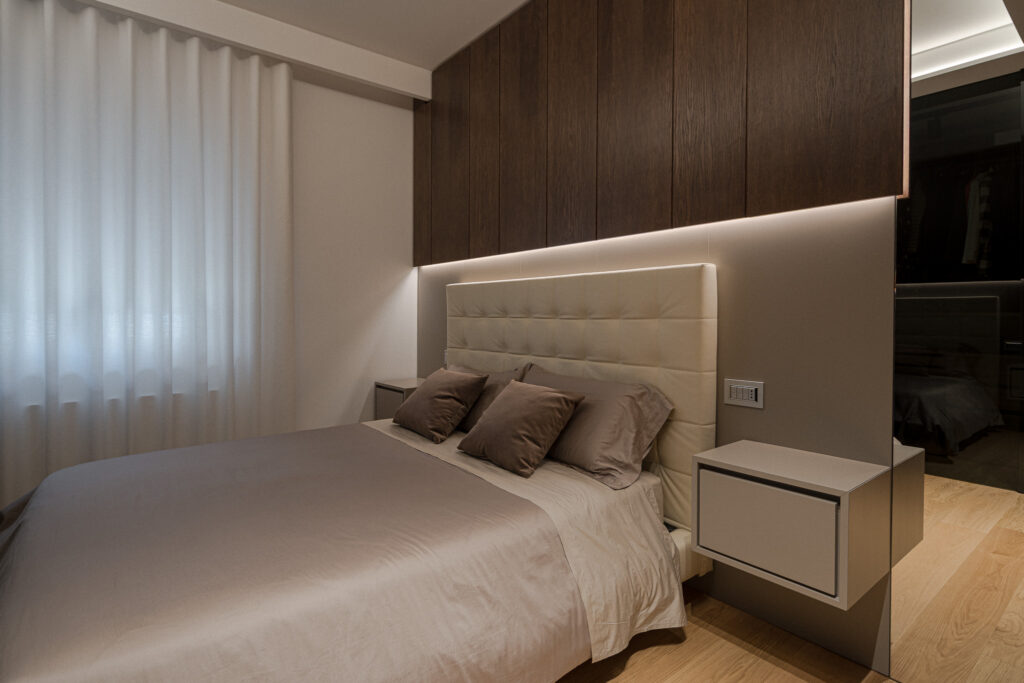 Camera con letto imbottito, comodino sospeso e armadiature in legno