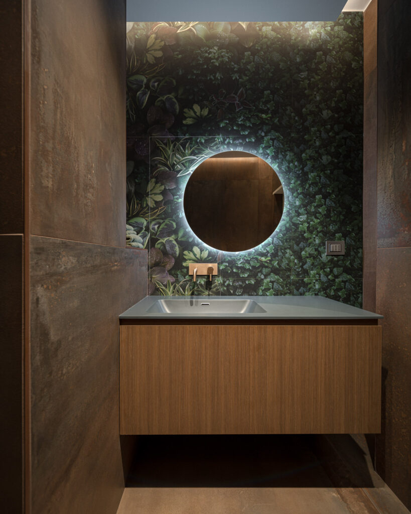 Mobile lavabo sospeso davanti a parete verde con specchio retroilluminato