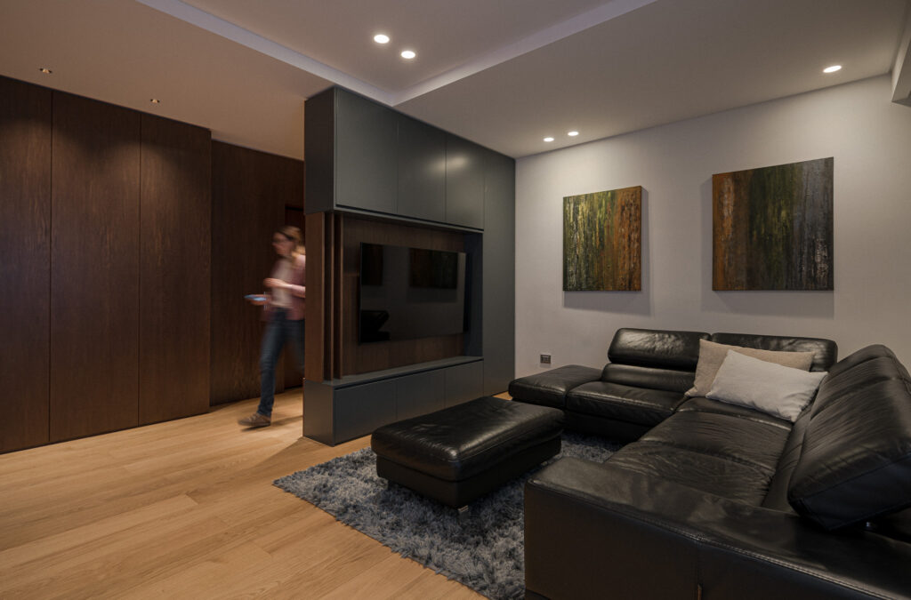 Living con parete TV in legno, divano nero e figura in movimento