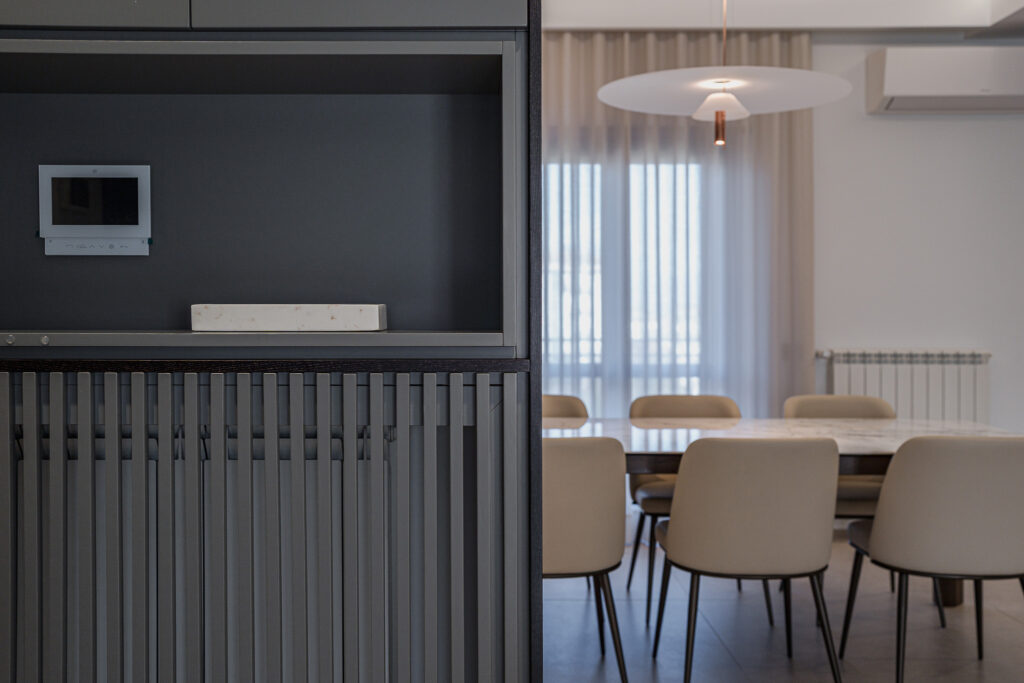 Parete attrezzata scura con videocitofono e sala da pranzo sullo sfondo