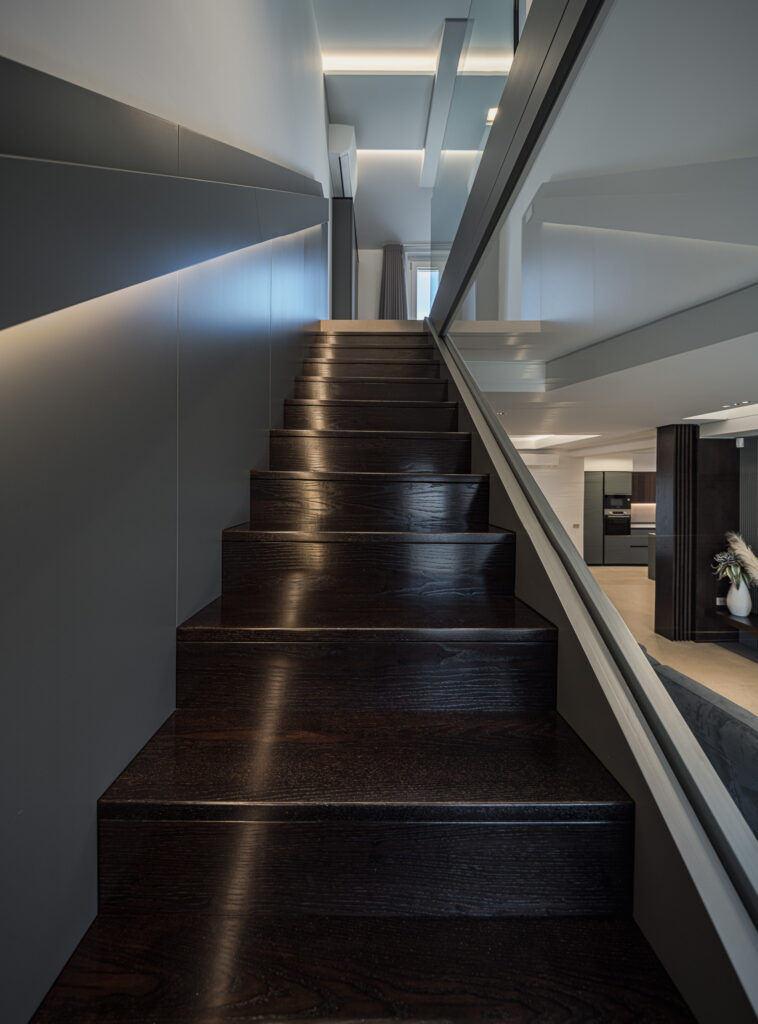 Scala in legno scuro con parapetto in vetro e illuminazione indiretta