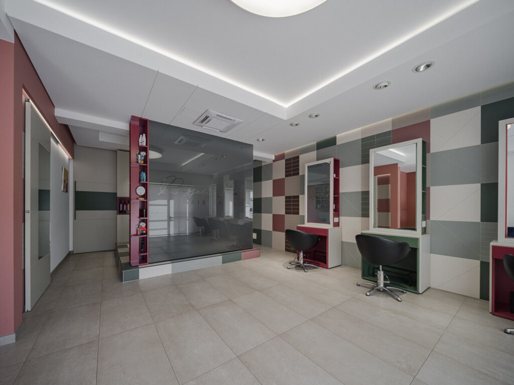 Interno del salone con postazioni parrucchiere, parete geometrica e vetro fumé
