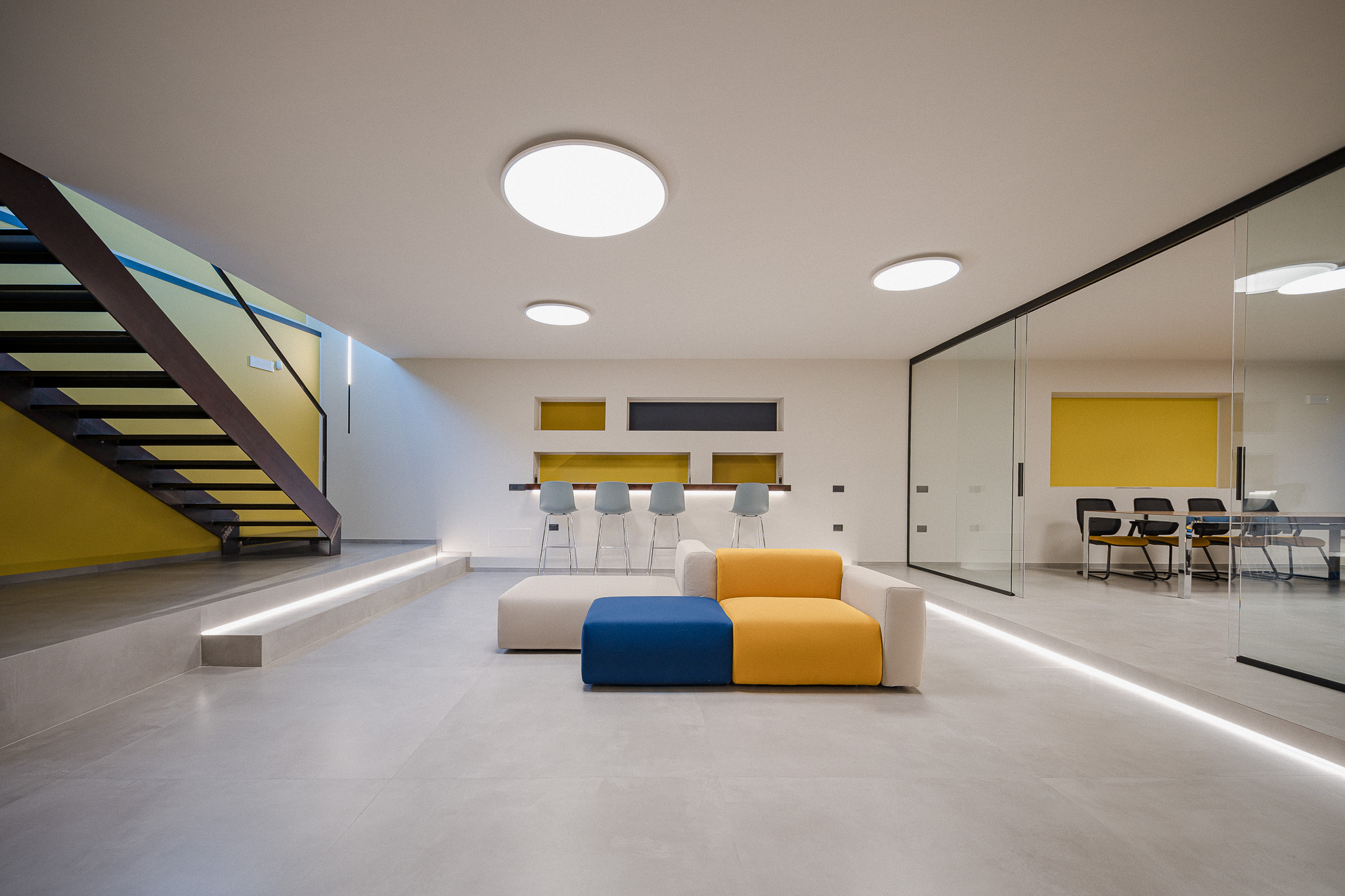 Divano modulare bianco, giallo e blu davanti alla sala riunioni vetrata