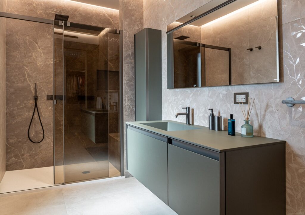 Bagno con mobile lavabo verde, grande specchio e doccia vetrata