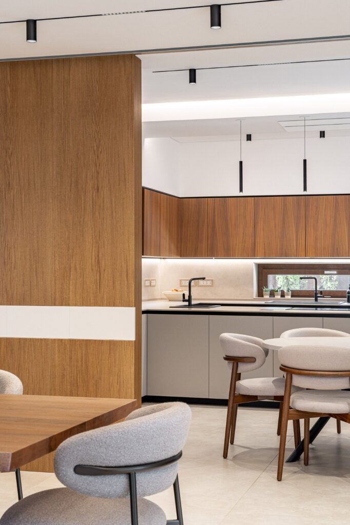 Zona pranzo con parete in legno e cucina visibile sul fondo