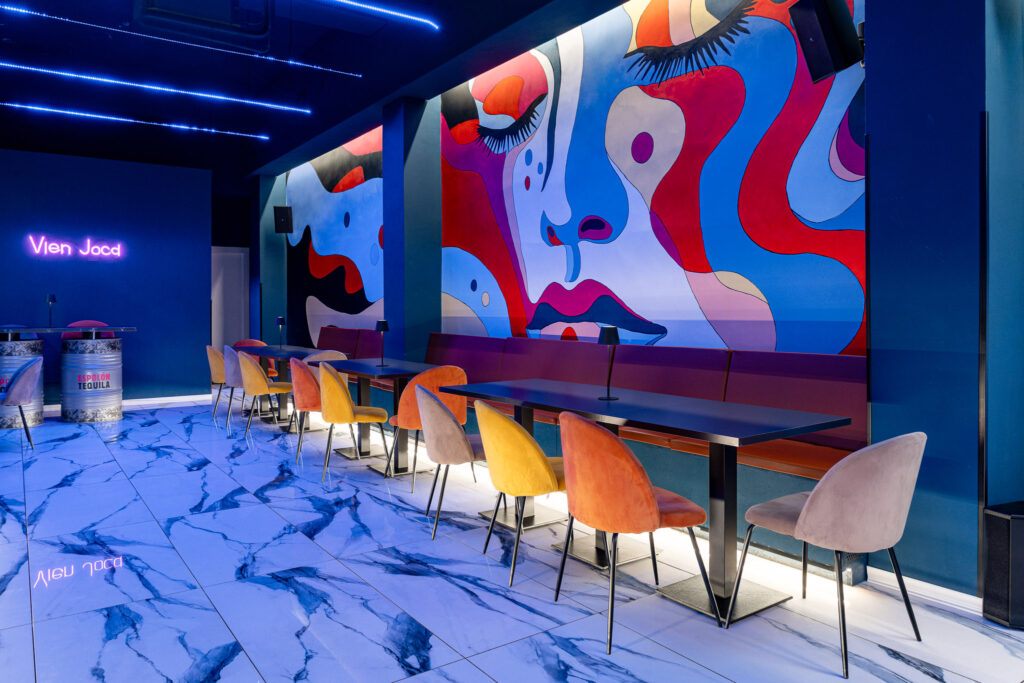 Sala del Drink Hub con grande murale Pop, divanetto e sedute colorate