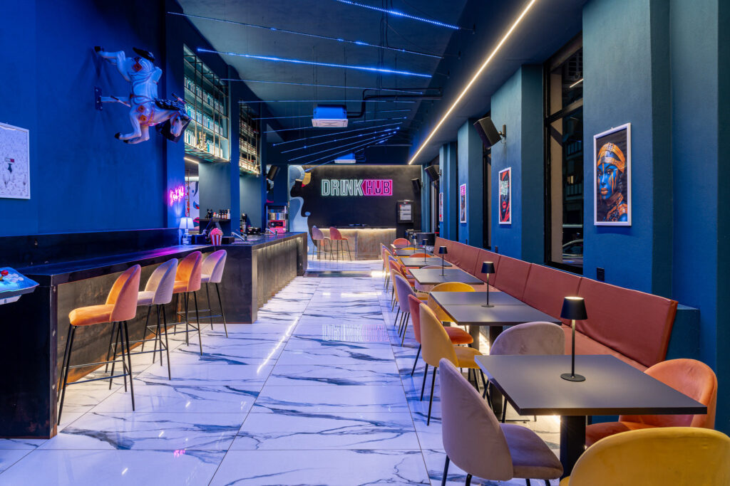 Vista del Drink Hub con bancone, cavallo decorativo, tavoli e postazione DJ