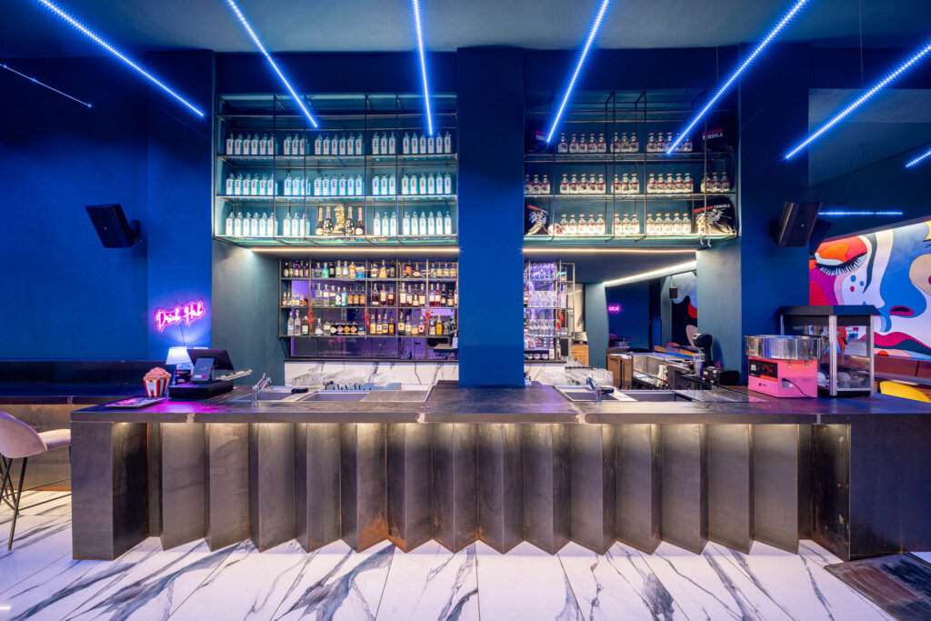 Bancone bar frontale con pannelli metallici piegati e bottigliere sospese
