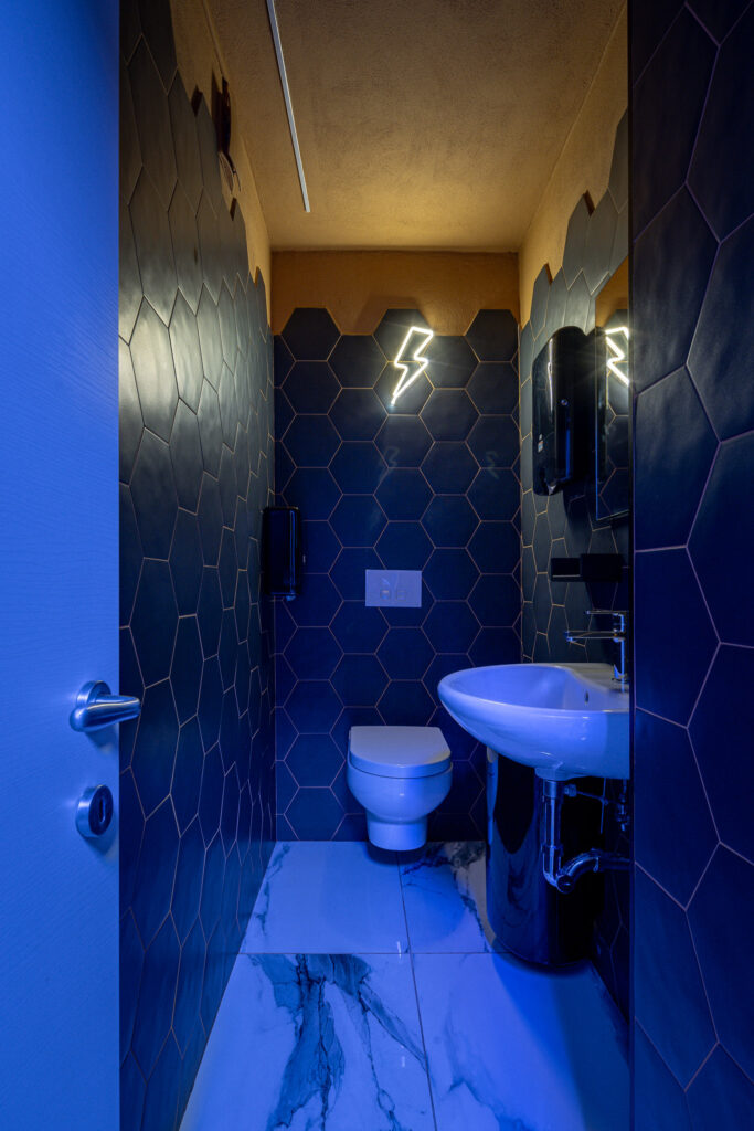 Bagno con pareti esagonali scure e illuminazione scenografica blu