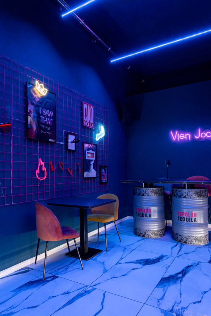 Parete a griglia con neon, immagini Pop e tavoli ricavati da fusti metallici