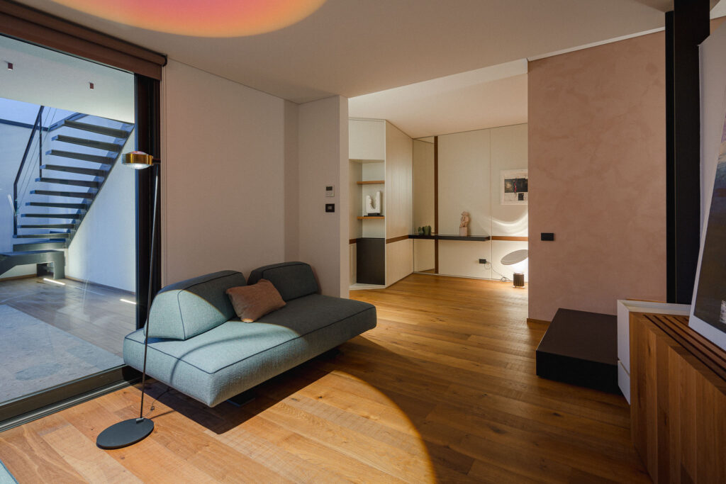 Living con divano modulare, parquet e ingresso illuminato sullo sfondo