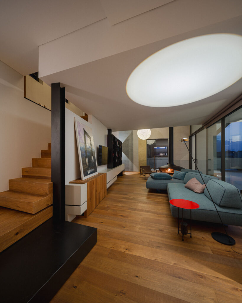 Scala in legno accanto al living con divano modulare e vetrata sulla terrazza