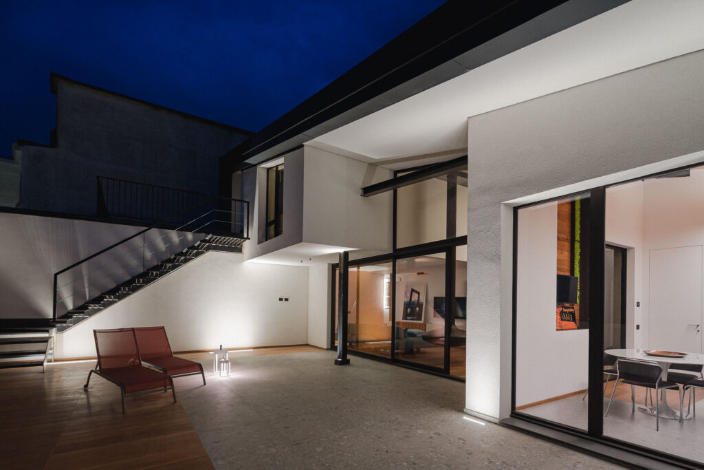 Terrazza serale con scala metallica, chaise longue e vetrate verso cucina e living