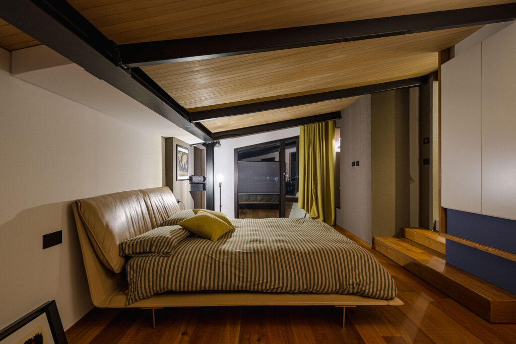 Camera padronale con letto imbottito, parquet e soffitto in legno con travi nere