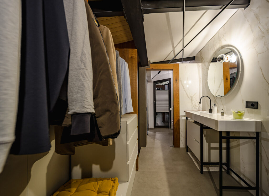 Bagno con lavabo sospeso e parete effetto marmo accanto alla cabina armadio aperta