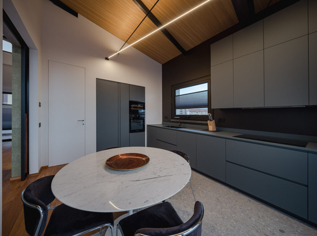 Cucina grigia con tavolo in marmo, travi nere e soffitto rivestito in legno