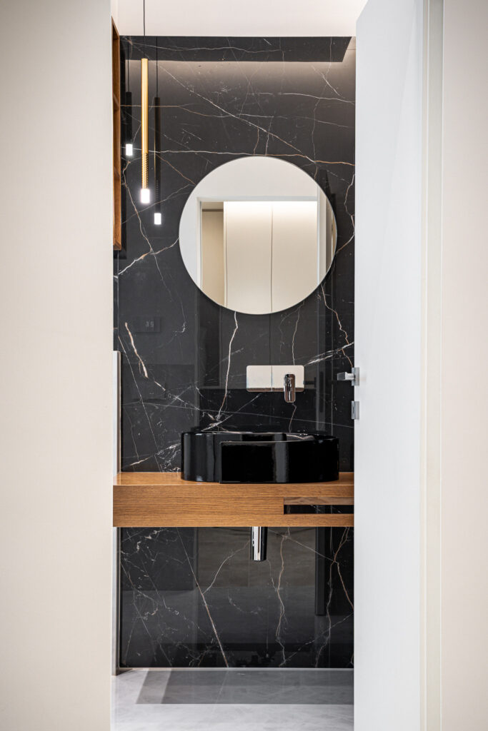 Bagno moderno con rivestimento effetto marmo nero, lavabo nero e piano in legno