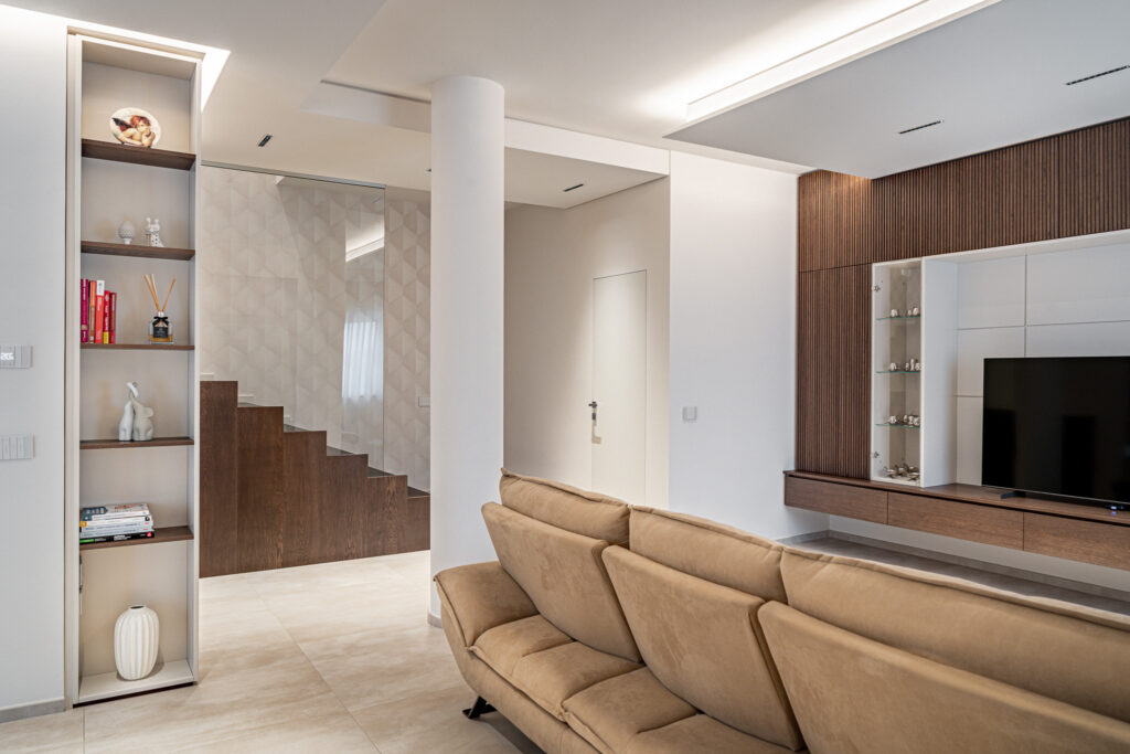 Soggiorno moderno con divano beige, parete TV in legno e scala interna