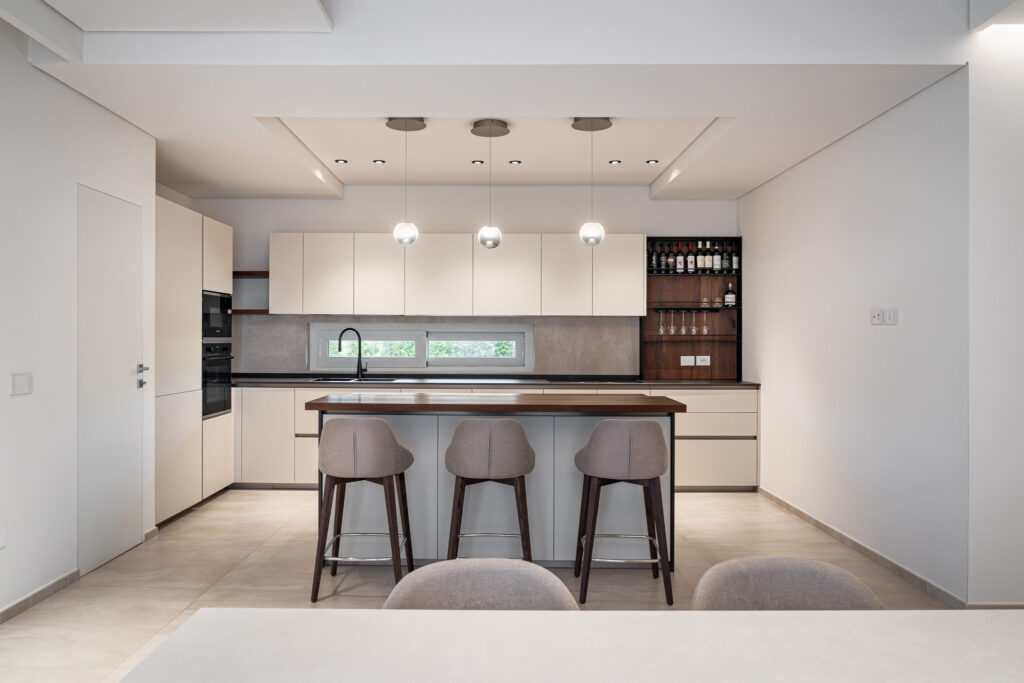 Vista frontale della cucina con isola, tre sgabelli e mobile bar in legno