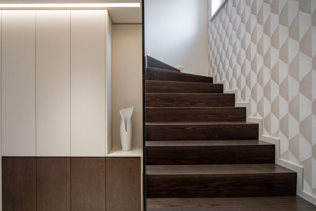 Scala interna in legno scuro con parete geometrica e mobile contenitore su misura
