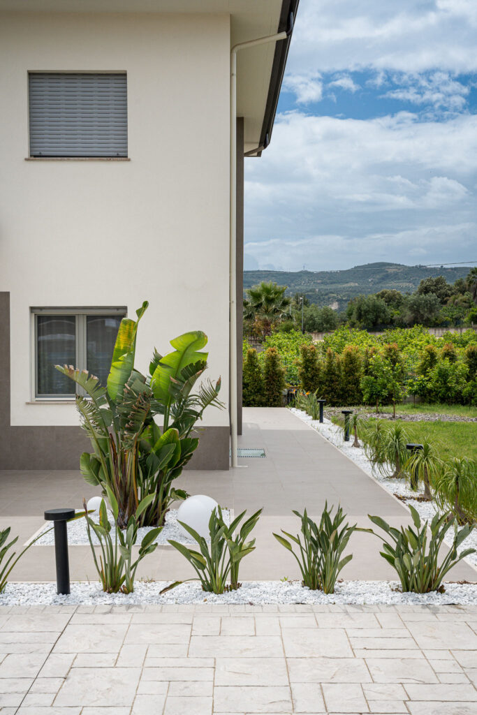Percorso pavimentato lungo la residenza con aiuole ornamentali e paesaggio collinare