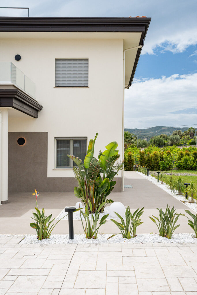 Facciata laterale della villa con aiuola tropicale e camminamento esterno